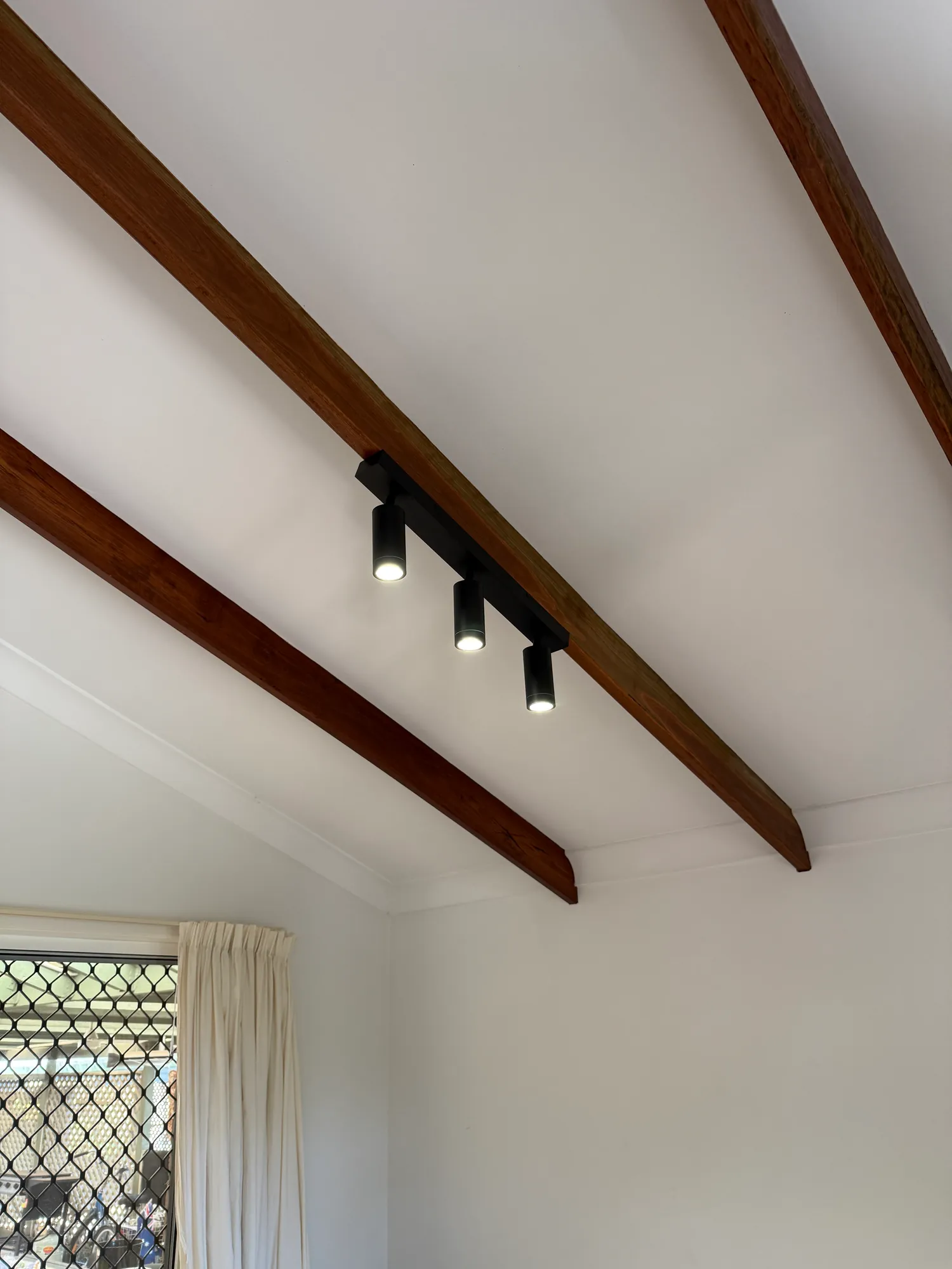 A black track light with three heads fixed along a dark timber ceiling beam