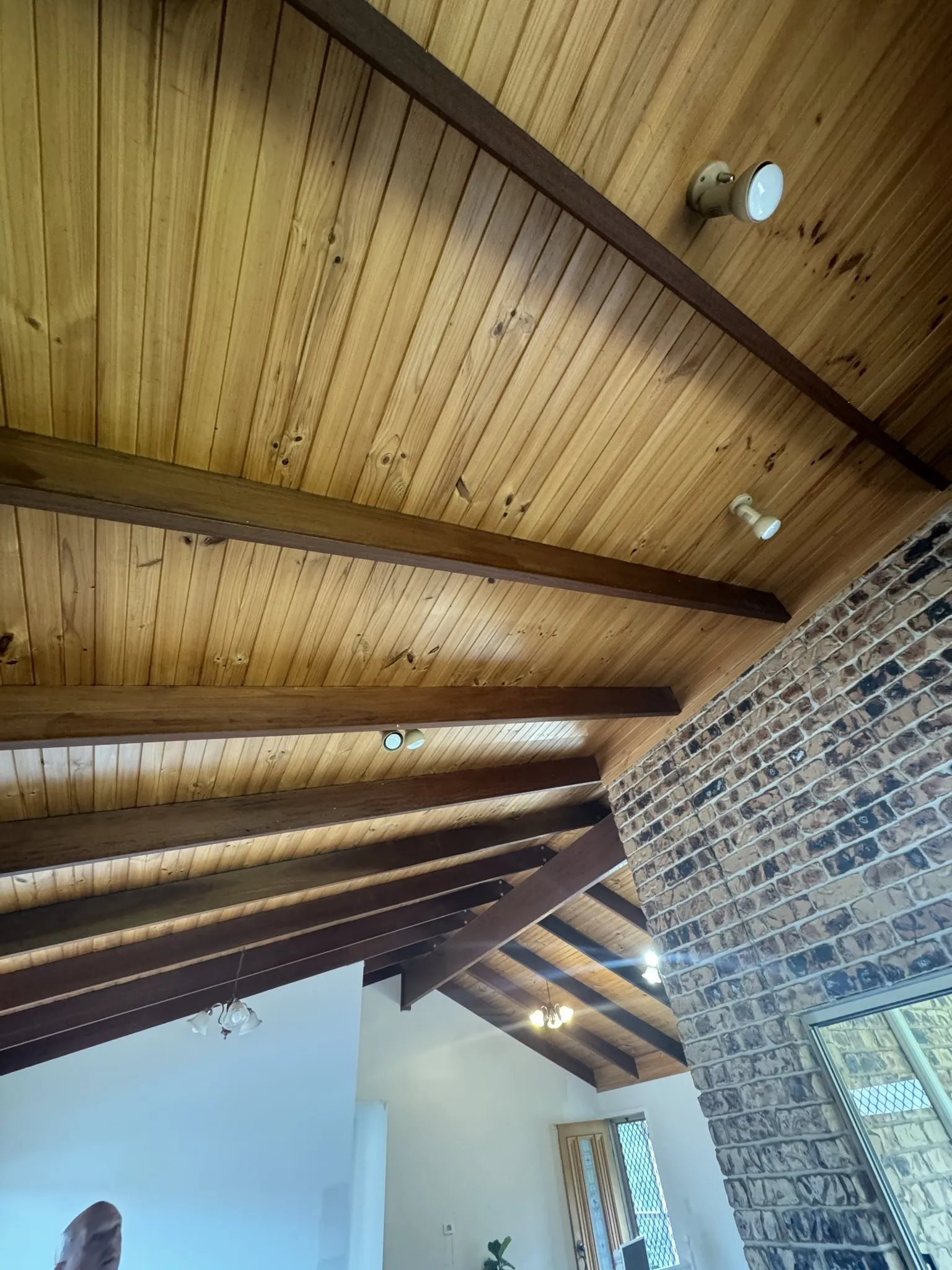 Lighting upgrade in a heritage Toowoomba home. The dated chandelier and spots on the timber raked ceiling were replaced with modern black track bar lighting and a matching black ceiling fan. Ceiling roses elsewhere preserved with LED downlights.