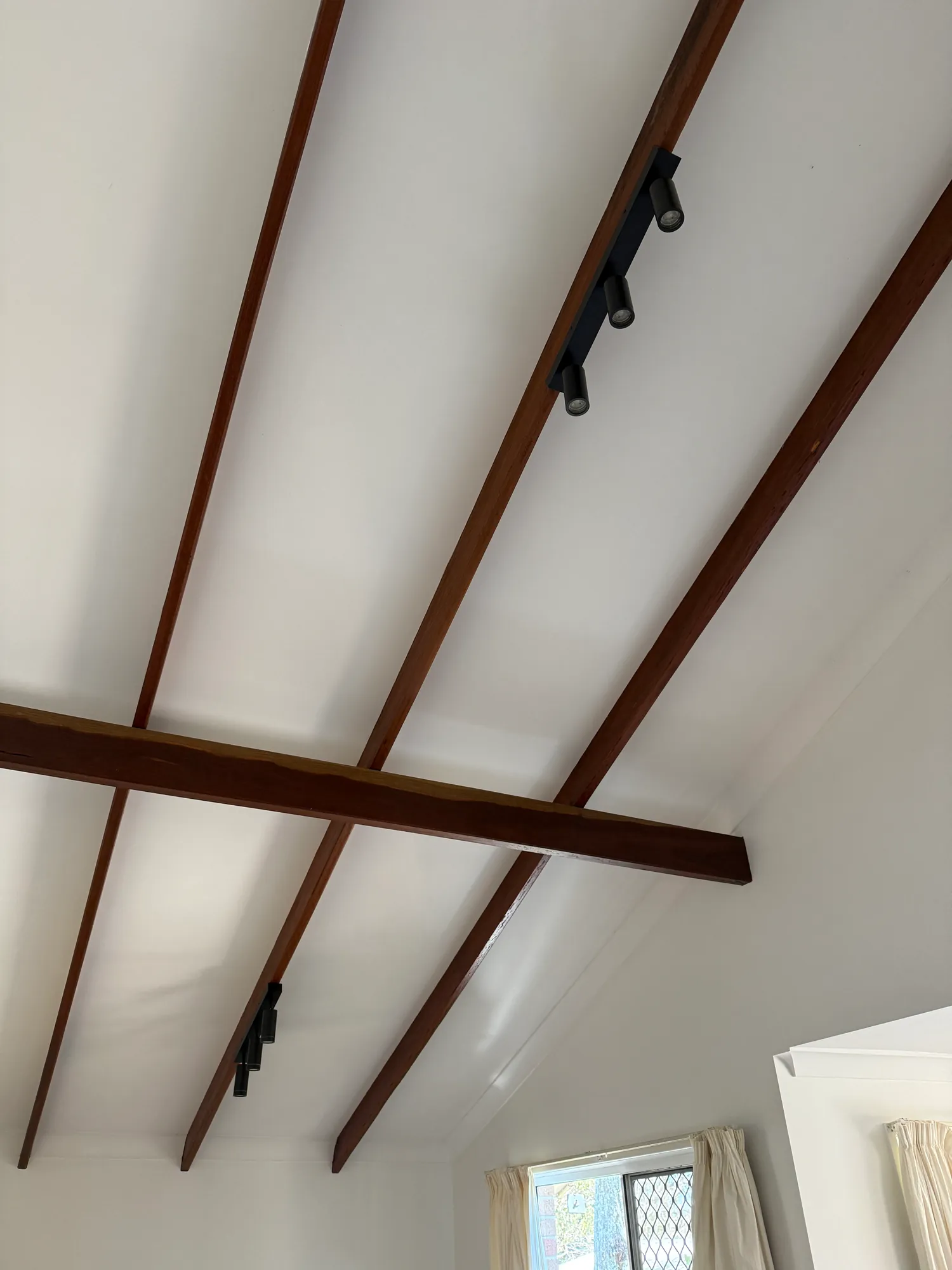 Black track lights on two timber beams across a raked white ceiling