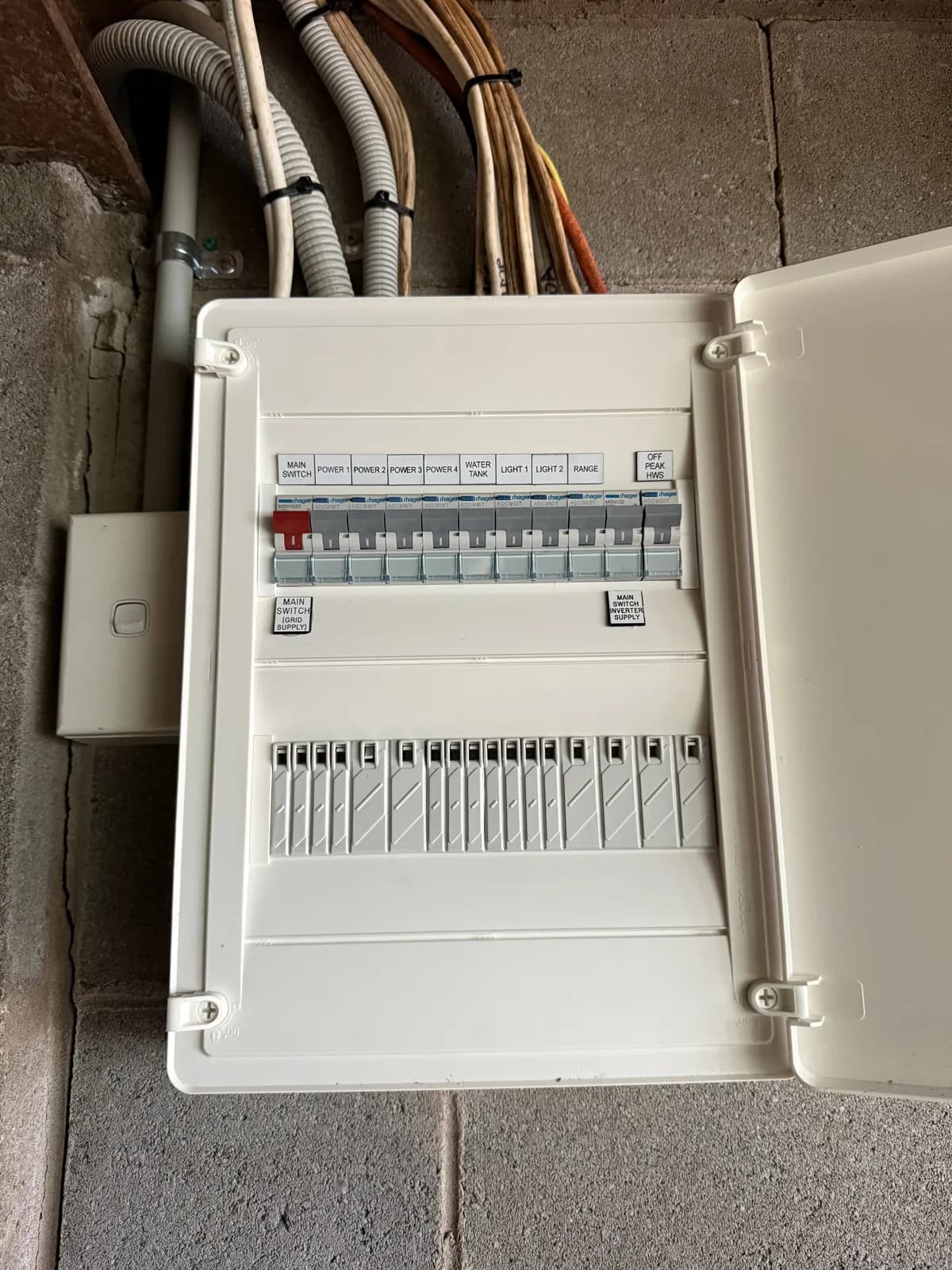 Exposed panel with ageing fuses upgraded to a fully enclosed switchboard with safety switches on every circuit. Before and after on the same blockwork wall.