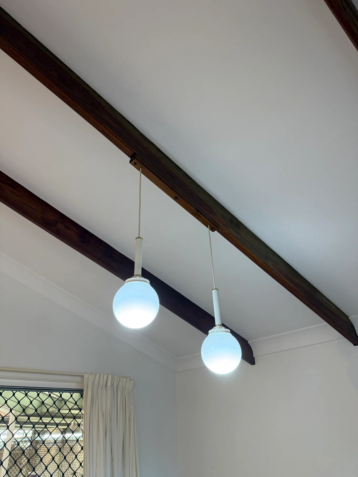 Two white globe pendants hanging from a raked ceiling with dark timber beams