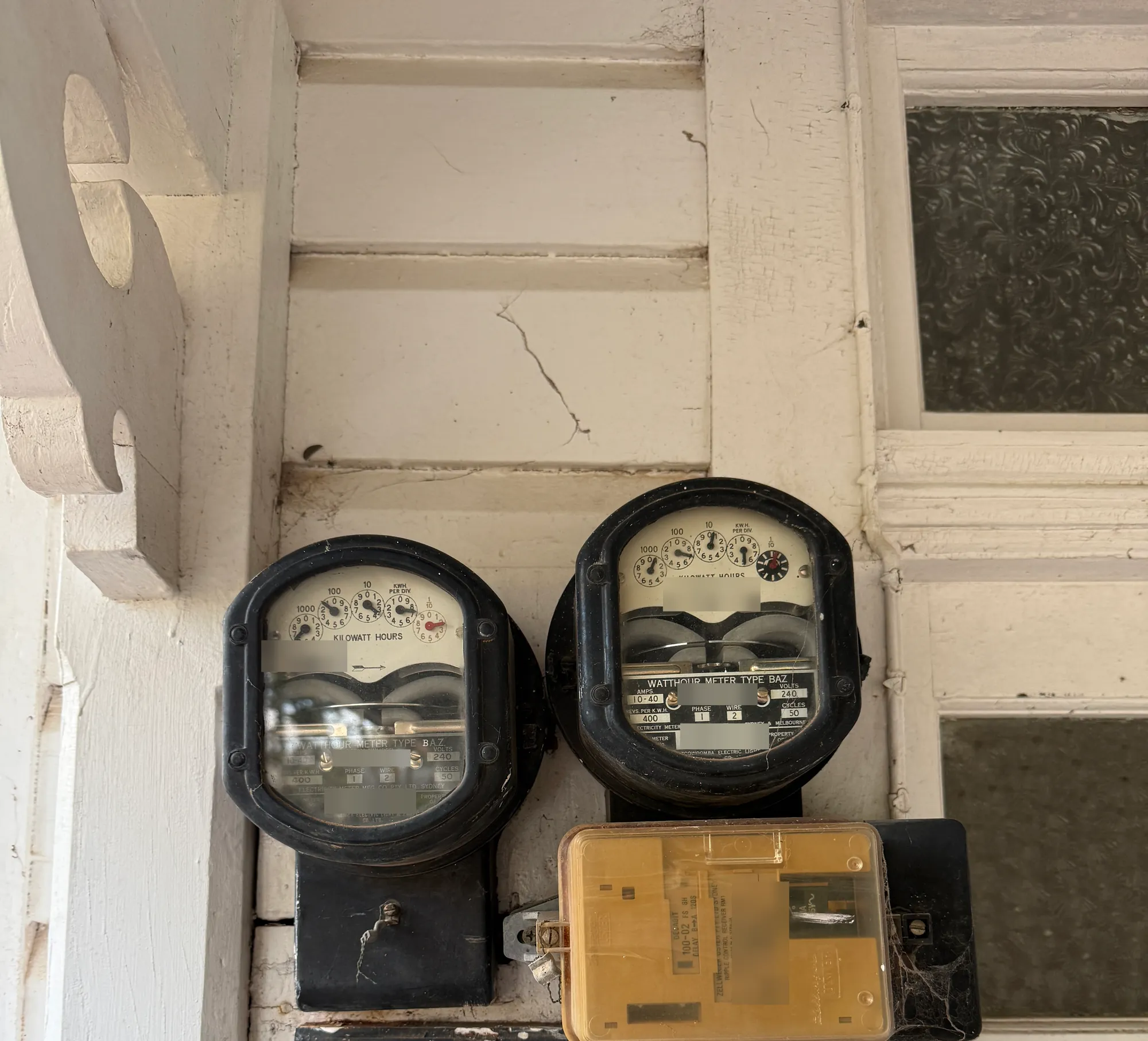 Two old dial meters and a ripple control relay on a painted timber veranda wall