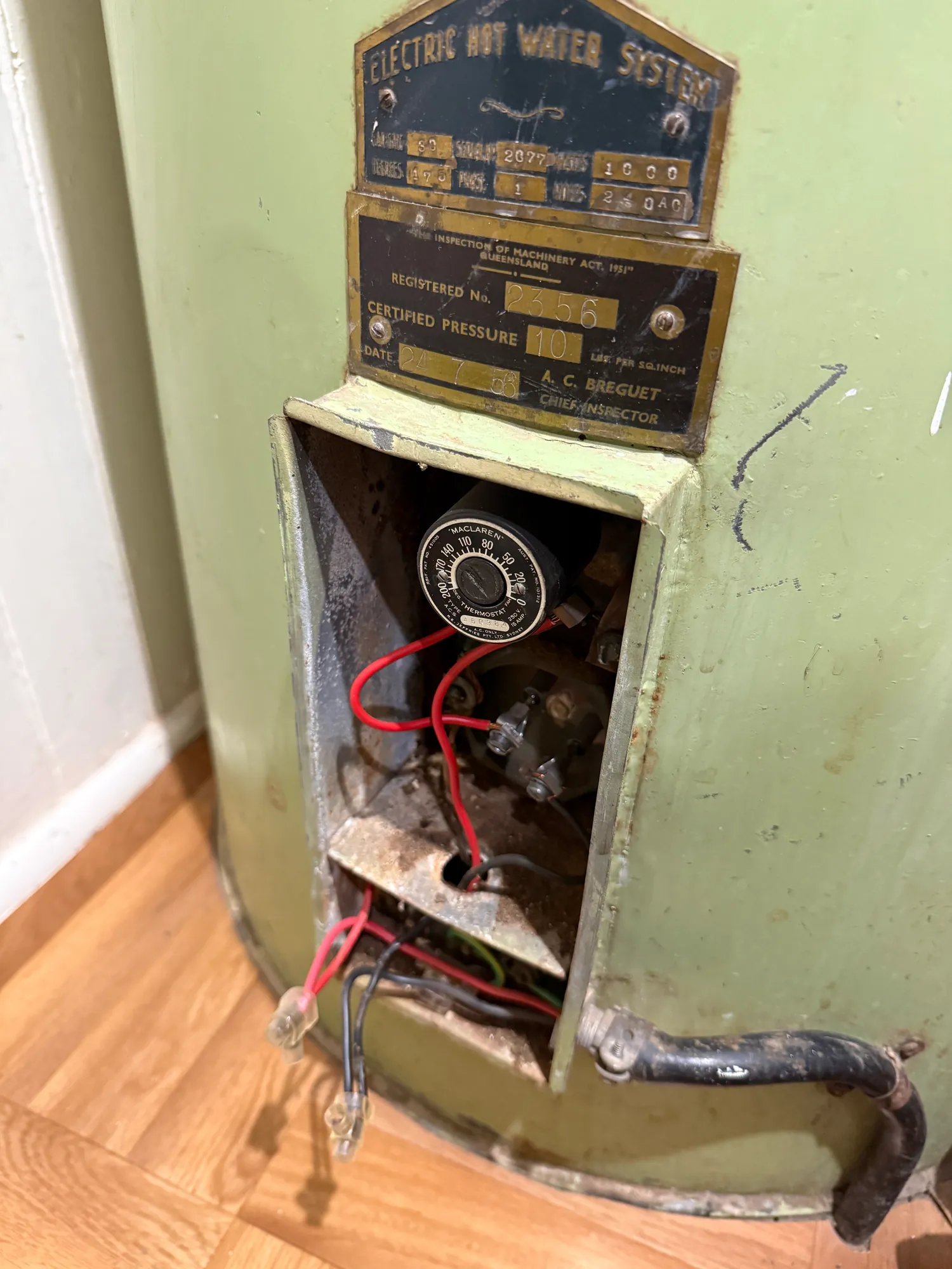 An old electric hot water unit with the lower access cover removed, showing the thermostat and wiring