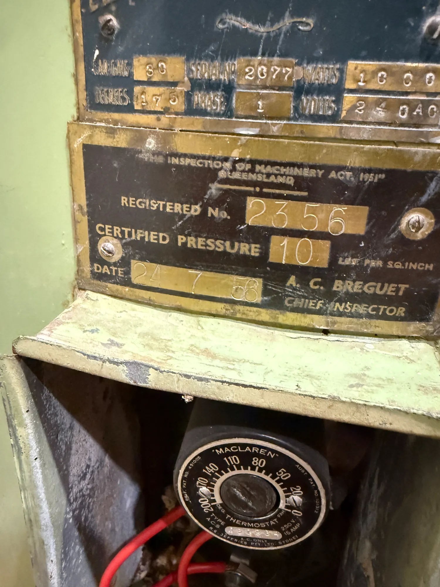 Brass inspection plate on an old electric hot water unit, above a Maclaren thermostat with its access cover off