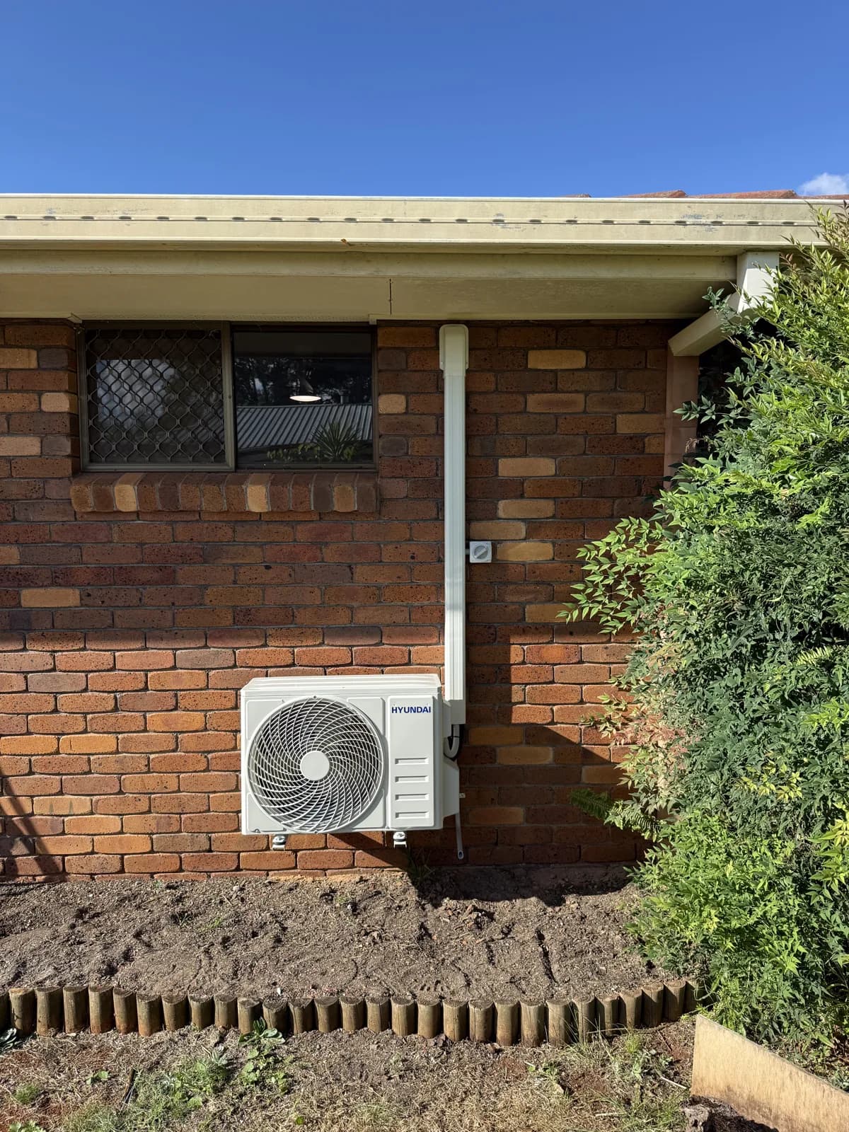 Bedroom split system installation with the outdoor unit tucked along the side of the house and all electrical connections weatherproofed.