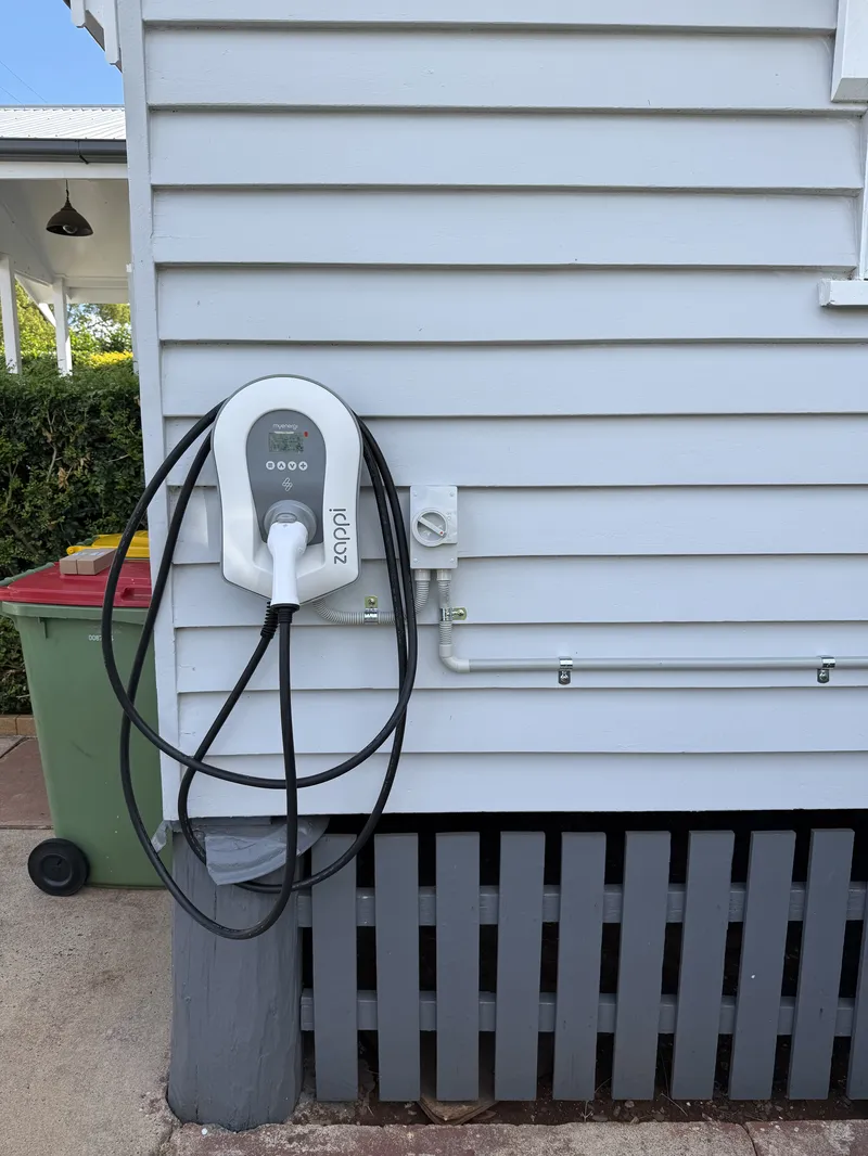 Zappi smart EV charger mounted on an exterior clapboard wall with a dedicated circuit run back to the switchboard. Solar-compatible charging for home electric vehicle use.